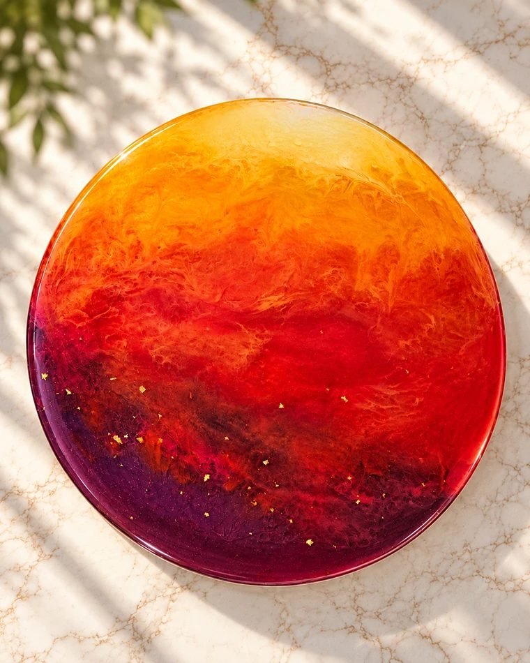 Pieza circular de resina con un degradado de naranja y rojo a púrpura, con destellos dorados, que evoca un atardecer